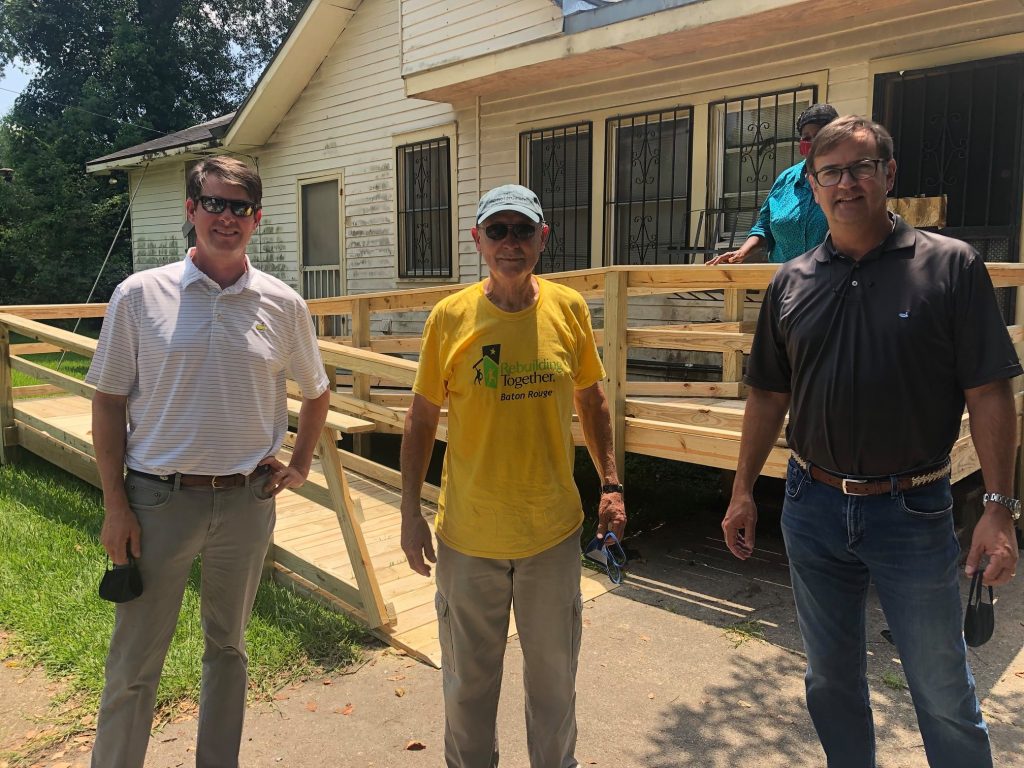 three men standing in front of a newly built wheelchair ramp