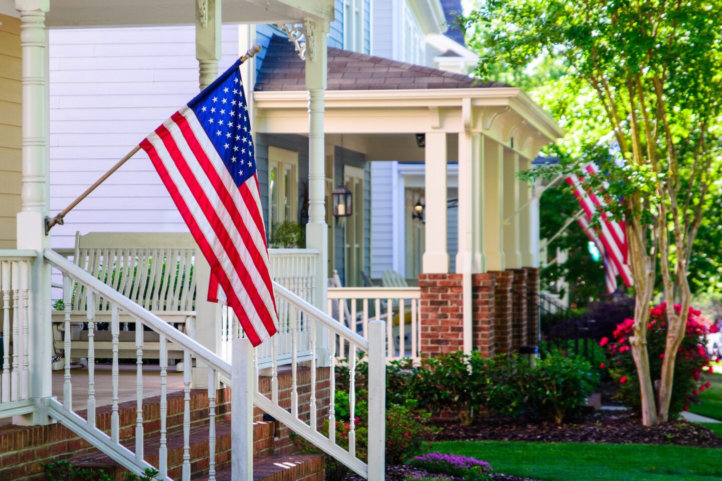American flags flying from two front porches with trees in view