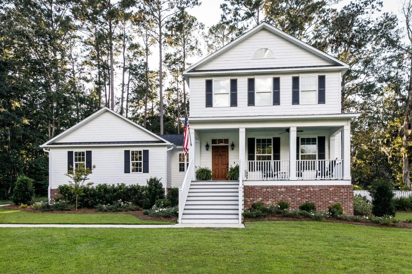 Rural two story white home with navy shutters and green grass front yard and trees in background
