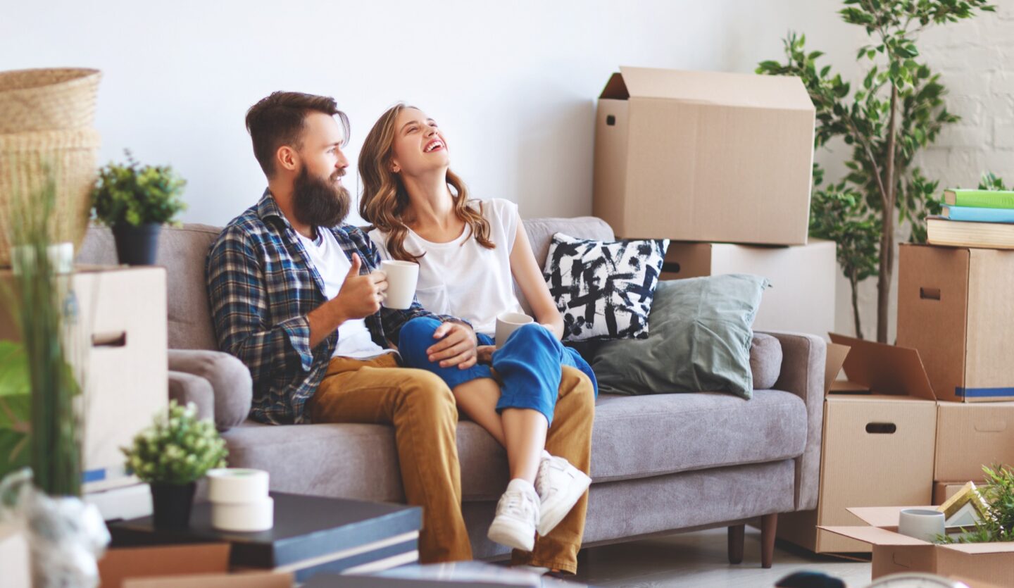 young couple sitting on couch in their first home unpacking moving boxes