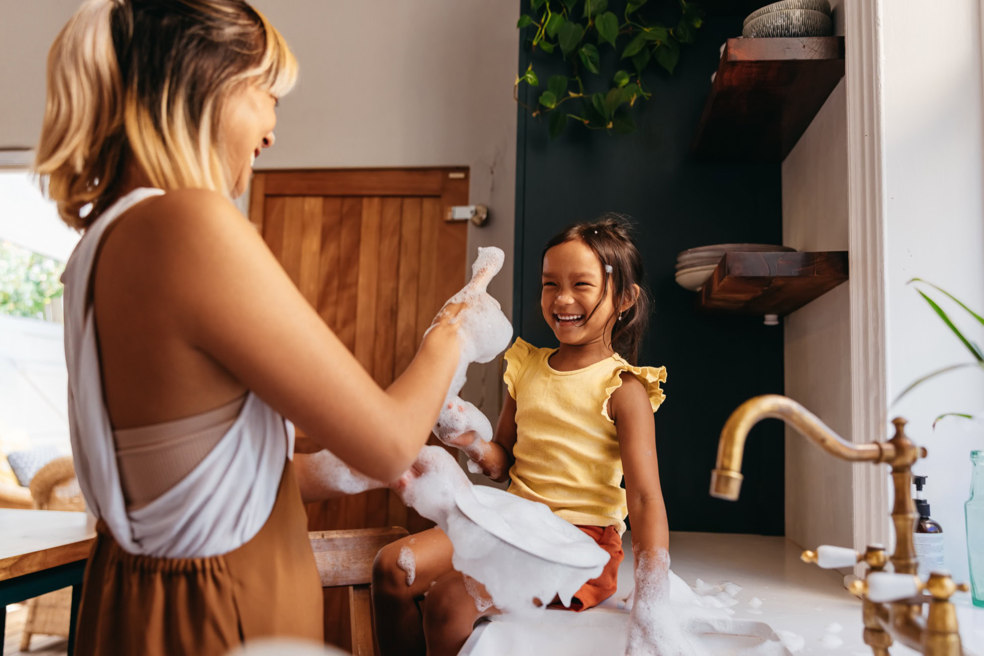 Mom and daughter having fun with soap foam in the kitchen