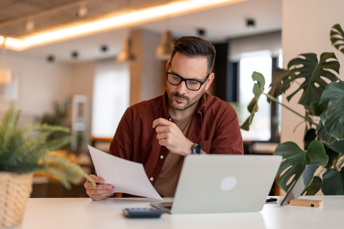 Man looking at paper in front of laptop