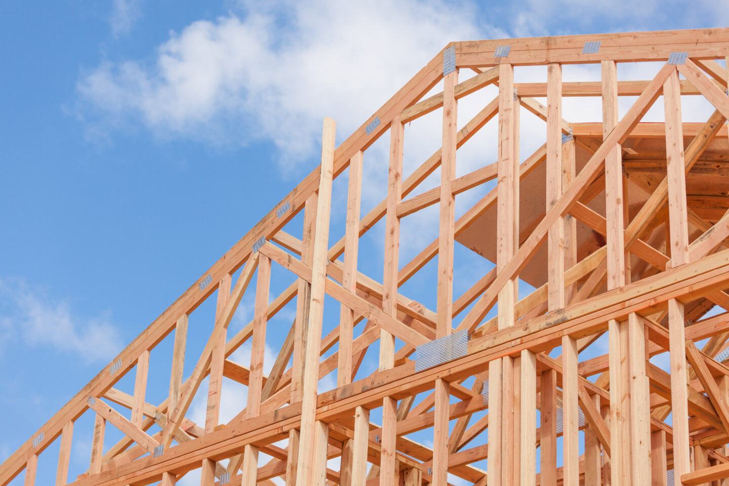 Wood beams on new construction home against blue sky and white clouds
