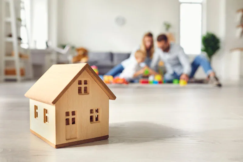 Graphic depicting a model house in the foreground with a family playing in their home's den in the background